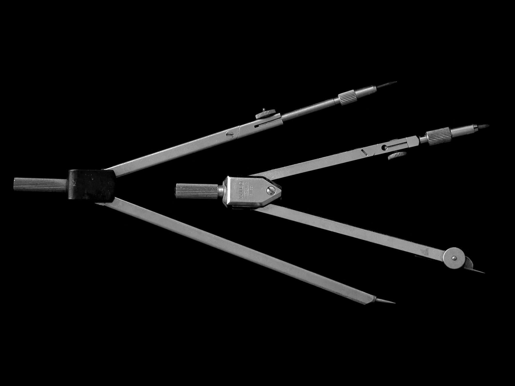 A pair of drawing compasses photographed against a black background